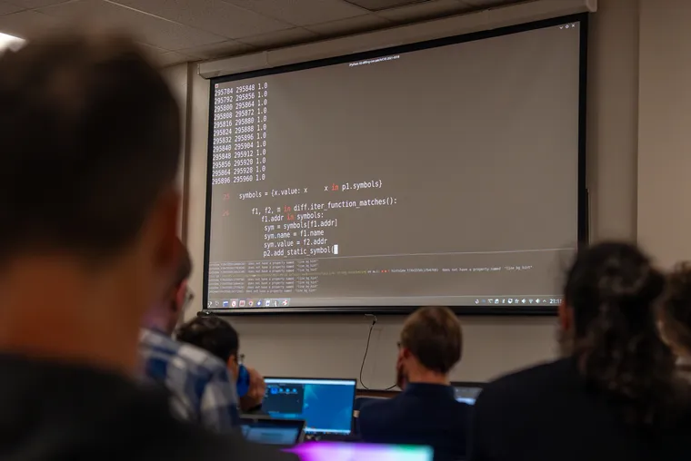 A classroom environment showing a large terminal on a projected screen with what looks like python code.